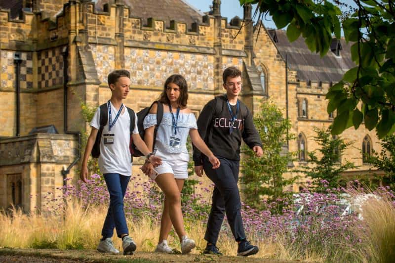 Three students walking outside in the grounds of their UK university college campus whilst at summer school