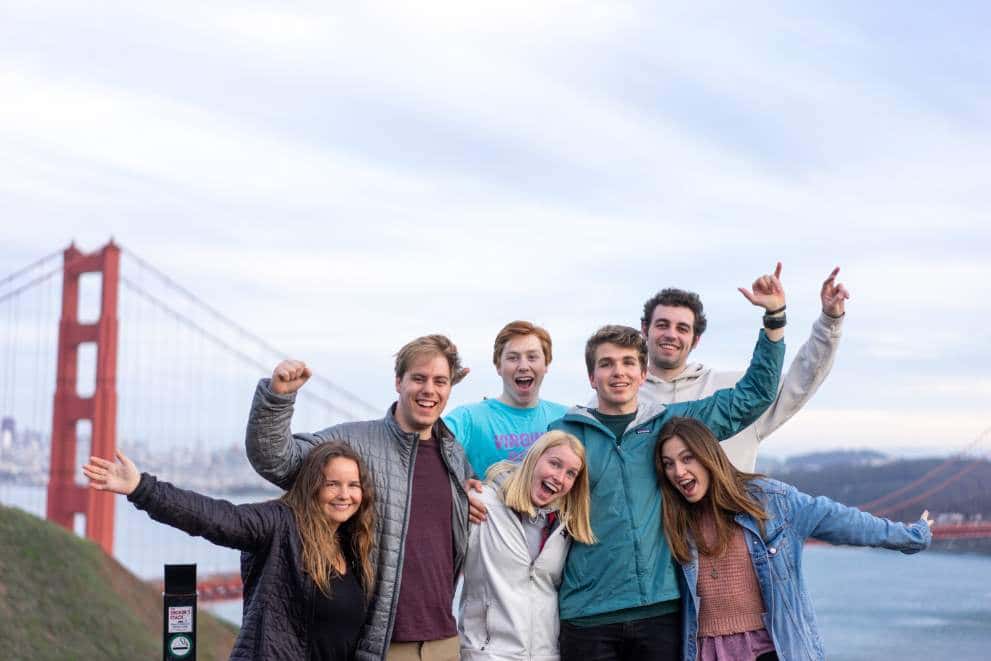 A group of summer school students smiling and posing for a photo in front of the Oaklands Bay Bridge in San Francisco, USA