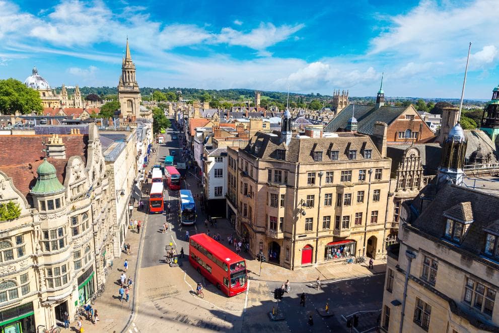 Oxford high street, UK, with several double decker red buses driving along it.