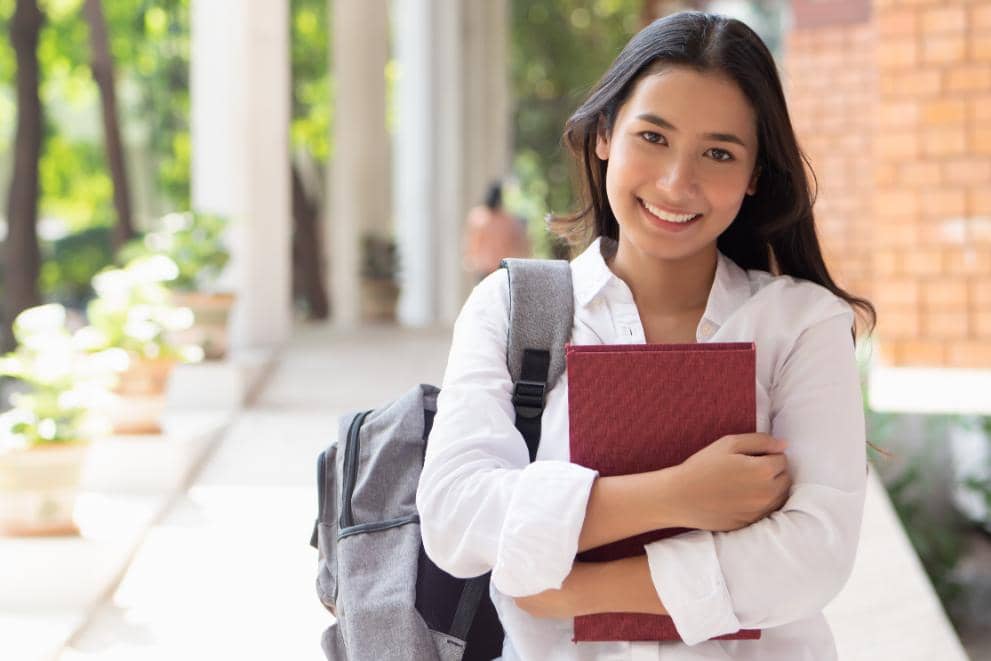A female summer school student hugging a red study book and smiling
