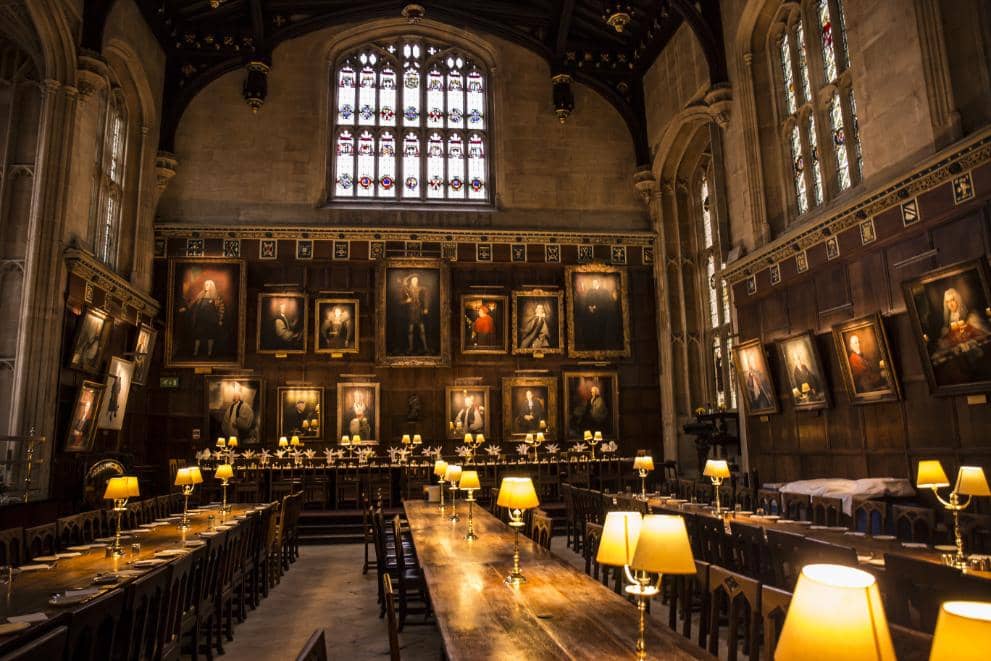 The inside of a traditional Oxford university college dining hall, lit by lamps in the evening
